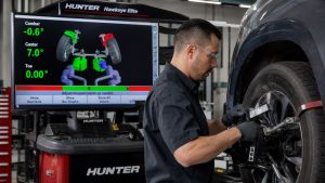 A professional technician using the Hunter Engineering Hawkeye Elite digital imaging system to perform a precision wheel alignment on a modern vehicle, with a monitor displaying 3D suspension geometry data.