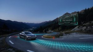 A modern, high-tech vehicle driving on a curved mountain road with a digital grid overlay on the asphalt and a dashboard inset showing a zero-degree steering baseline